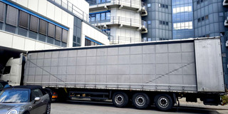 Auf dem Foto sieht man einen grauen LKW vor einer Häuserreihe stehen.