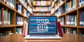Foto: Auf einem Tisch in einer Bibliothek steht ein Laptop, auf dessen Bildschirm ein Buch-Icon abgebildet ist.