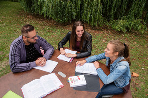 Studierende Studierende sitzen um einen Tisch im freien und arbeiten.