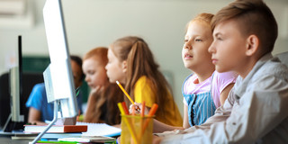 The picture shows children sitting at computers from the side.