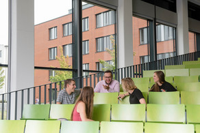 Studierende im Hörsaal Fünf Studierende sitzen in einem Hörsaal und unterhalten sich.