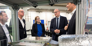 Foto: Mehrere Personen diskutieren an einem technischen Gerät hinter Glas.